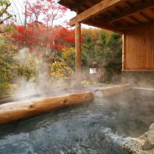 Steaming outdoor onsen bath with wooden beams and autumn maple trees at Aishinkan, Iwate