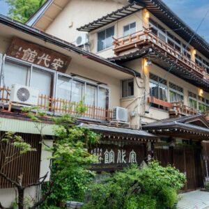 Multi-story traditional ryokan facade with wooden balconies and greenery in Nagano's Chūbu region