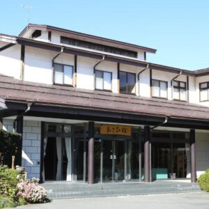 Two story ryokan facade with tiled roof, glass doors and manicured shrubs at Asahikan in Nagano Chubu