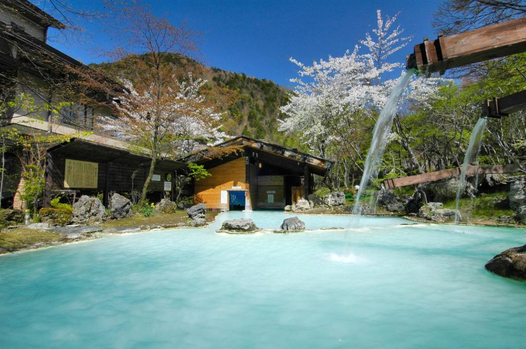 Outdoor onsen at Awanoyu Nagano Milky turquoise outdoor onsen at Awanoyu with wooden spout, rock edge, traditional buildings and blossoming tree in Nagano