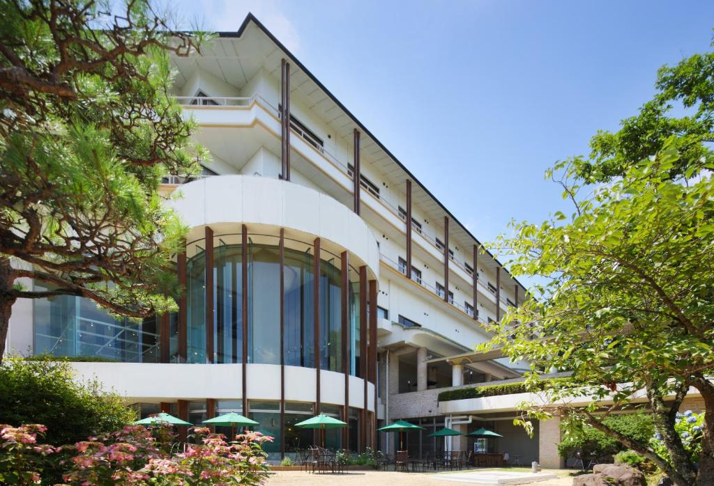 Modern ryokan exterior Azumakan Fukushima Tōhoku White multi-story ryokan with curved glass facade, balconies, outdoor umbrellas and surrounding trees in Fukushima