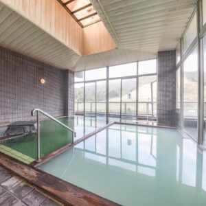 Milky onsen pools inside tiled bathhouse with large windows overlooking grassy hills at Bousenkaku Niigata