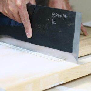 Hands cutting fresh noodles with a wide Japanese knife on a wooden board