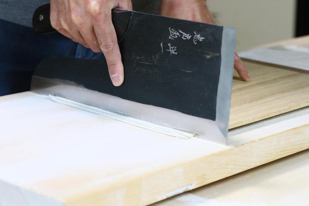 Noodle cutting demonstration Fukuichi Chūbu Yamanashi Hands cutting fresh noodles with a wide Japanese knife on a wooden board