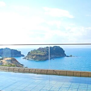 Outdoor onsen bath with tiled edge and glass railing overlooking islands and blue sea at Futagojimasou, Wakayama
