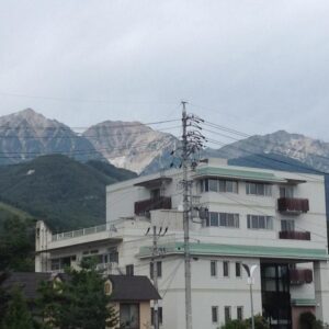 White multi-story ryokan building with balconies and mountain range backdrop in Nagano, Chūbu