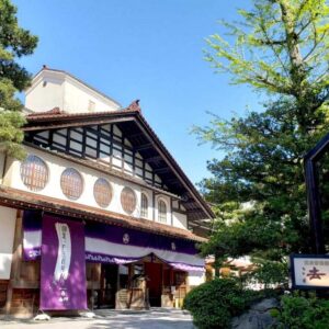 Entrance of Hoshi ryokan with purple noren, wooden facade and trees in Ishikawa, Chūbu region