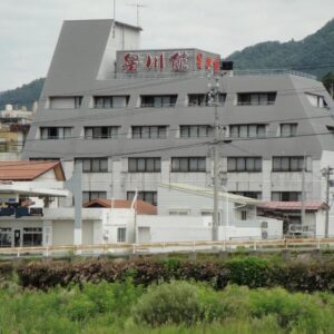 Multi-story riverside ryokan building with signage and mountain backdrop in Nagano Chūbu region