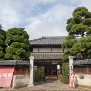 Ryokan entrance with tiled roof, noren and kimono-clad guest at Iizukatei, Tochigi