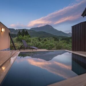 Wooden outdoor onsen bath reflecting sunset with mountain view and deck chair, Ikkoten ryokan, Ōita, Kyūshū