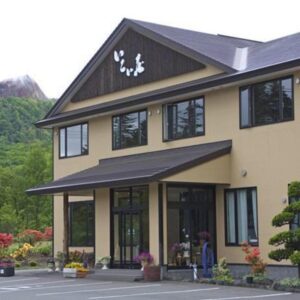 Exterior view of two story ryokan building and landscaped entrance with distant mountain backdrop in Hokkaidō