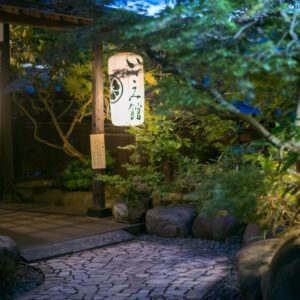 Lantern-lit stone path leading to Isamikan entrance in Tochigi, surrounded by trees and traditional lanterns