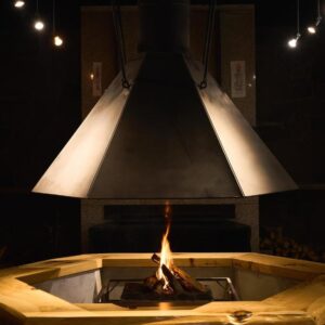 Central wooden irori hearth with suspended metal hood and glowing fire at Ishinoyu Lodge in Nagano