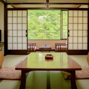 Tatami room with low table, shoji screens and veranda overlooking green foliage at Issinkan, Tochigi, Kantō, Japan