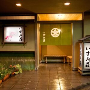 Warm lantern-lit ryokan entrance with noren curtain, wooden bench, potted plants and tiled entry at Izumi-so, Gifu, Chūbu
