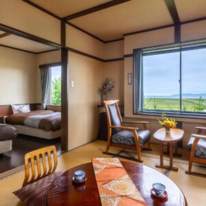 Tatami floor room with low table, chairs and two beds by a large window overlooking a distant landscape