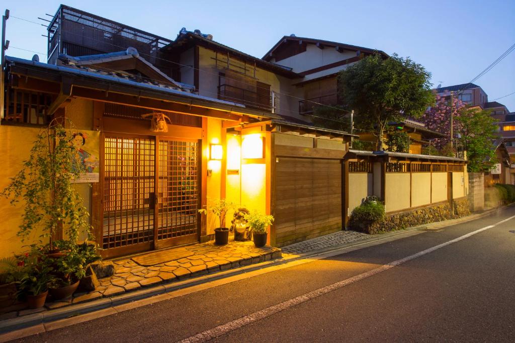 Lit ryokan entrance Kamuroan Kyoto Warm lit wooden entrance with shoji doors and potted plants along a quiet Kyoto street at dusk