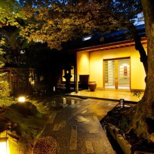 Stone walkway and lanterns leading to Kocho ryokan entrance amid trees in Ishikawa, Chūbu, Japan