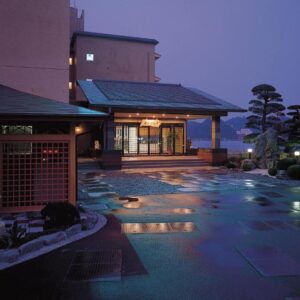 Lit entrance with wet stone courtyard and stone lantern beside manicured trees at Kochoran in Mie