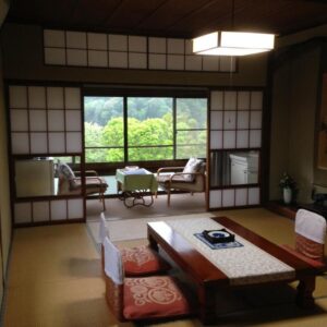 Tatami room with low table, zabuton cushions, shoji screens and verdant view through large window at Kofukan, Niigata