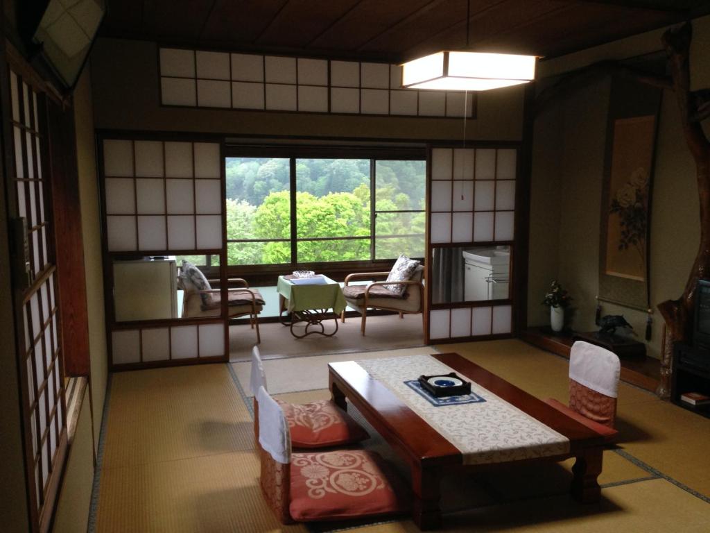 Tatami Sitting Room at Kofukan Niigata Tatami room with low table, zabuton cushions, shoji screens and verdant view through large window at Kofukan, Niigata