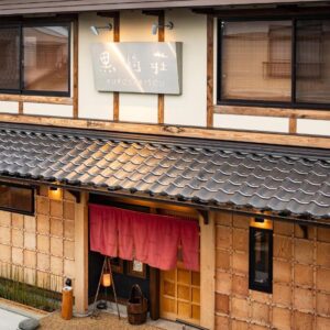 Traditional wooden ryokan entrance with red noren, tiled roof and shoji windows at Kurosakisou in Kyoto