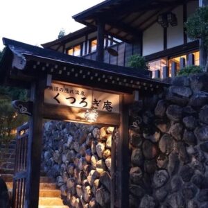Lit wooden gate and stone wall entrance with steps leading to Kutsurogian ryokan in Niigata