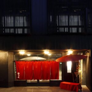 Dimly lit ryokan entrance with red noren curtains and lantern at Manten-no-Hoshi in Kanagawa