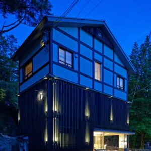 Dusk exterior of three-story timber ryokan with illuminated entrance and surrounding trees in Hiroshima prefecture