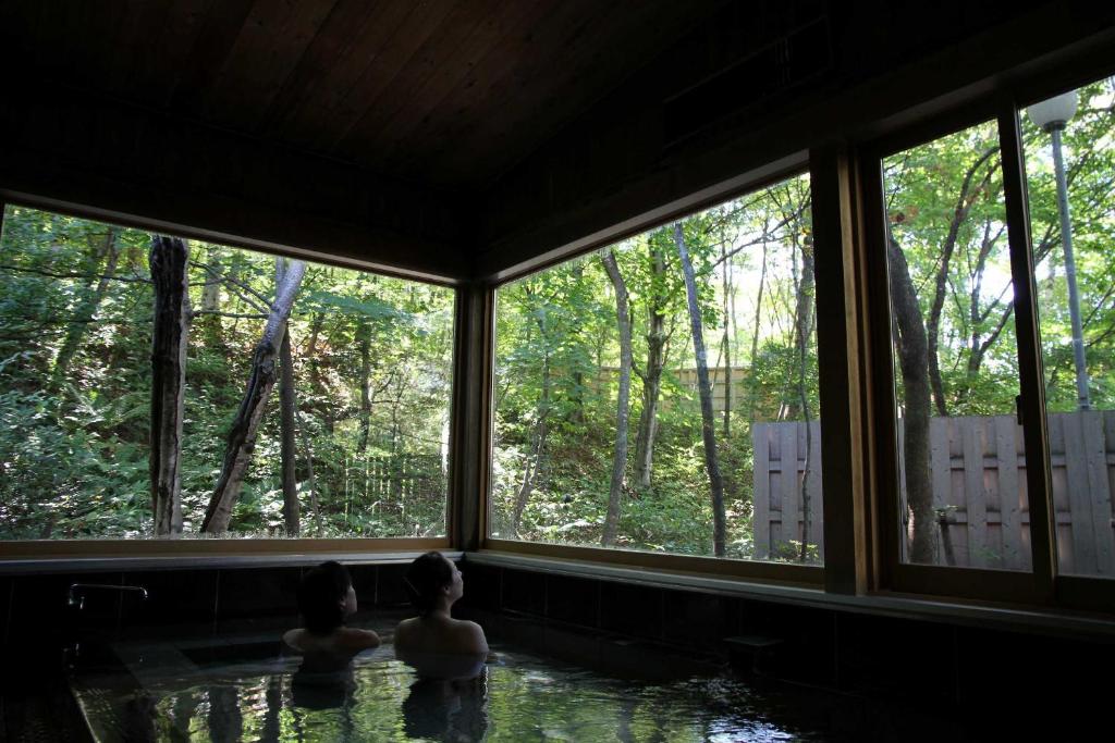 Forest-view indoor onsen Nakaodaira Gifu Indoor onsen bath with wide windows revealing lush forest, wooden interior, guests seated in the water