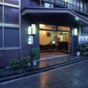 Wet evening street and lit entrance showing reception area at Nisshokan ryokan in Mie, Kansai