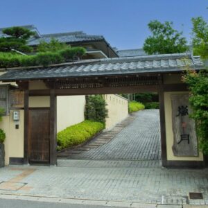 Wooden entrance gate with tiled roof and stone driveway leading to Rangetsu ryokan in Kyoto