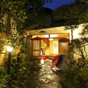 Stone lantern-lit garden path leading to Sansuisou entrance with umbrellas and wooden doorway in Kanagawa
