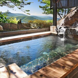 Wood-framed outdoor onsen with stone spillway and mountain views at Sawaemon in Chūbu Nagano