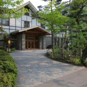 Stone driveway leading to Senjukaku wooden entrance surrounded by evergreen trees and traditional exterior in Nagano, Chūbu Japan