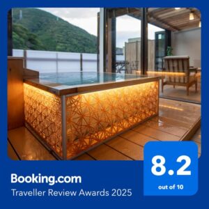 Illuminated wooden bathing tub with decorative panel, glass terrace doors and mountain view at Senkei ryokan, Kanagawa