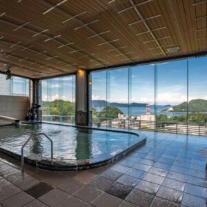 Spacious indoor onsen with large windows showing coastal hills, washing stools visible, Senpokaku, Mie, Kansai, Japan