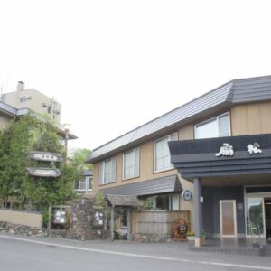 Entrance and facade of Senshoen ryokan on a quiet Hokkaidō street with greenery and neighboring buildings