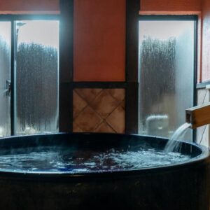 Round wooden soaking tub with steaming windows in intimate indoor onsen room at Sensui Hyōgo