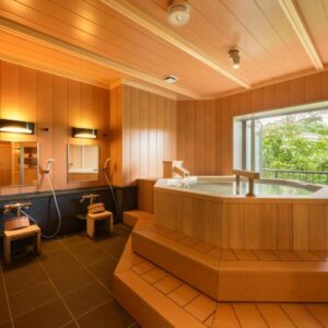 Indoor wooden soaking tub with stools and large window overlooking greenery at Shintomi-tei, Miyagi