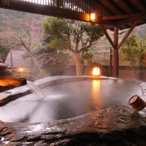 Steaming stone onsen with lanterns and wooden roof at Shirakabe, Shizuoka