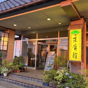 Lit entrance with signboard, potted plants and glass doors at Suehirokan in Niigata