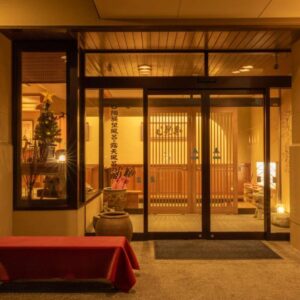 Entrance with sliding glass doors, wooden interior panels, lanterns and red bench at Suminoyu in Nagano