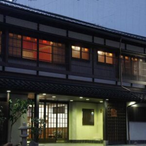Two-story wooden ryokan facade with lit shoji windows and entrance lantern at Sumiyoshiya in Ishikawa