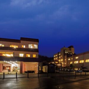 Lit multi-story ryokan exterior at twilight with paved forecourt and warm interior lights, Sumiyoshiya in Niigata Prefecture