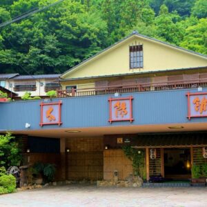 Yellow two-story ryokan facade with entrance and mountain backdrop at Taiyokan in Gunma, Kantō