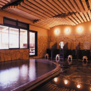 Indoor onsen with wooden ceiling, stone walls and washing stations at Ukiha ryokan in Ōita