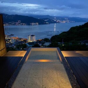 Stone outdoor onsen bath on terrace overlooking bay at dusk, Uminohana, Shizuoka, Chūbu