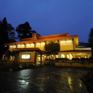 Evening exterior of Wakatake ryokan with lit facade, wet driveway and surrounding trees in Niigata, Chūbu region