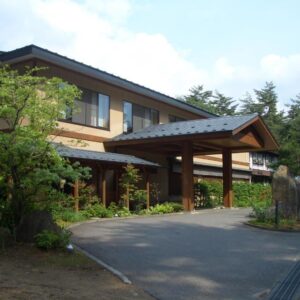Traditional two-story ryokan entrance with wooden portico, driveway and surrounding trees in Nagano's Chūbu region